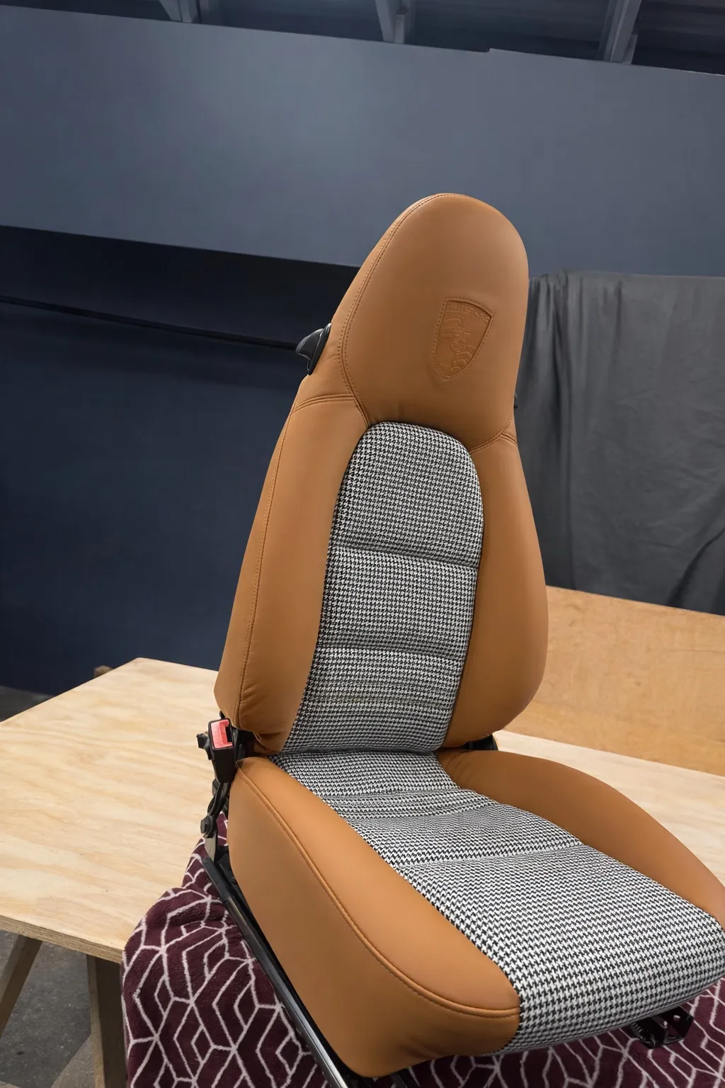 Finished Porsche Boxster S seat on the bench with saddle leather bolsters and houndstooth center.